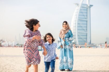 Nő és gyermekek játszanak a dubai strandon, háttérben a Burj Al Arab.