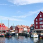 Színes vitorlás hajók a Skagen kikötőben, jellegzetes vörös raktárépületekkel.