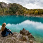 A nő ül a Rudabányai-tónál, türkizkék víz és hegyek környezetében.
